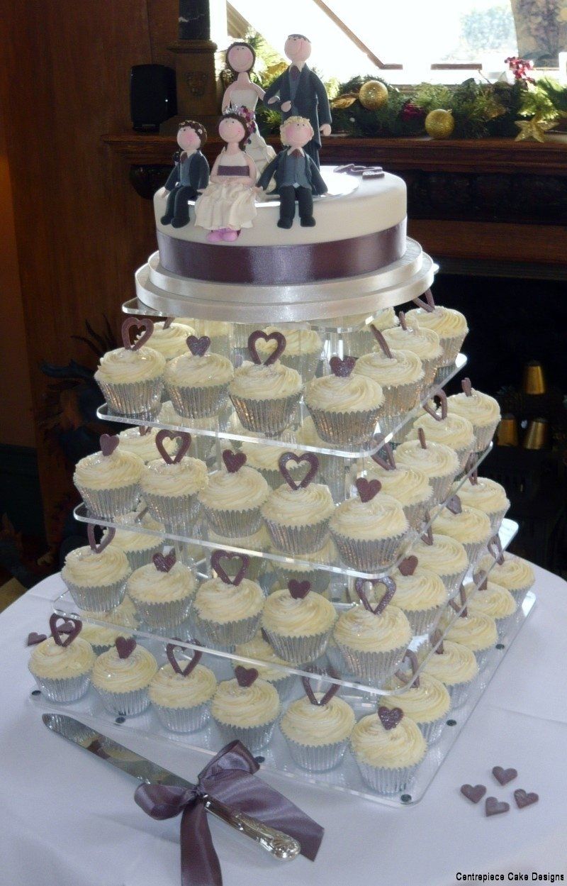 Wedding cake with tiered cupcakes and figurines on top. White frosting, purple accents, formal setting.