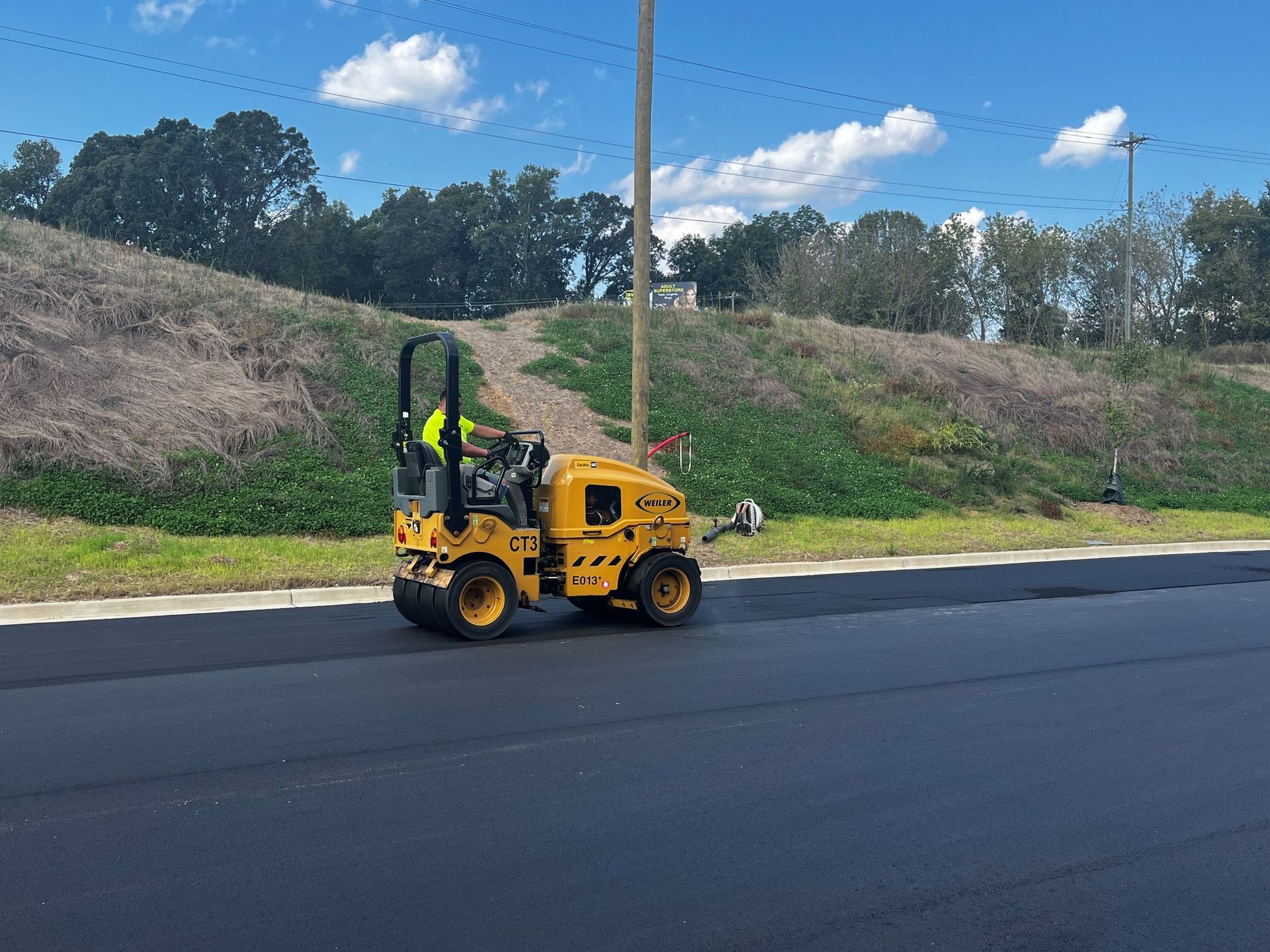 A yellow truck is driving down a road next to a grassy hill