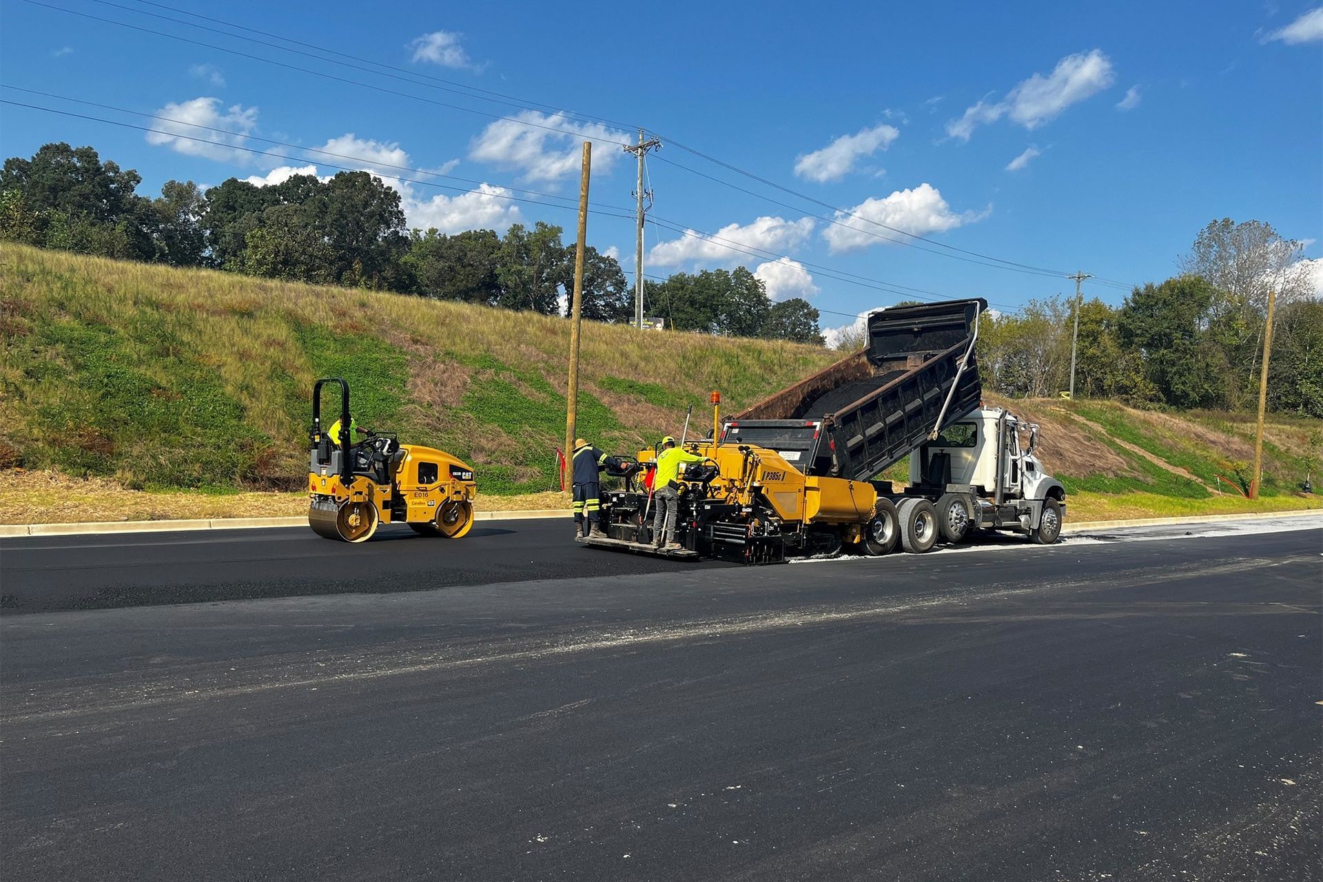 A dump truck is being loaded with asphalt on a road