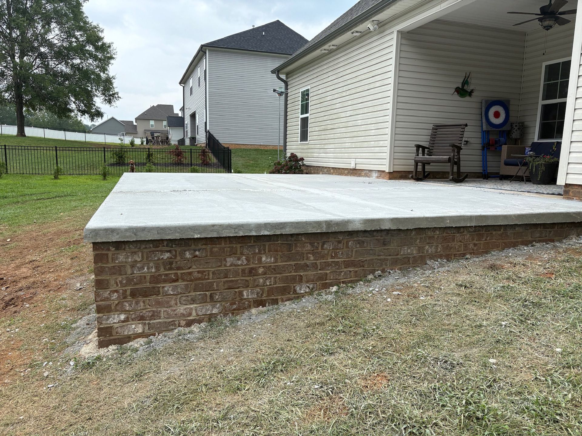 Brick patio platform beside a white house with covered porch and lawn.