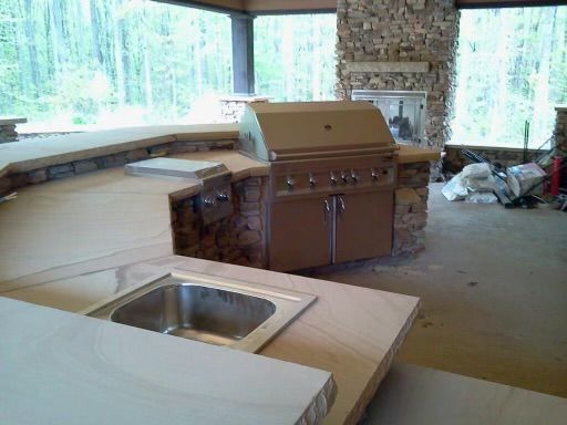 Unfinished kitchen with a granite island, stainless sink, and outdoor stone grill by large windows