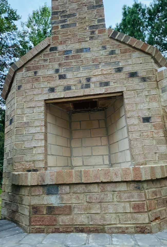 Stone outdoor fireplace with a brick chimney and open firebox.