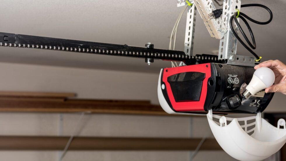 Person replacing a lightbulb in a garage door opener, red and white housing, black track.