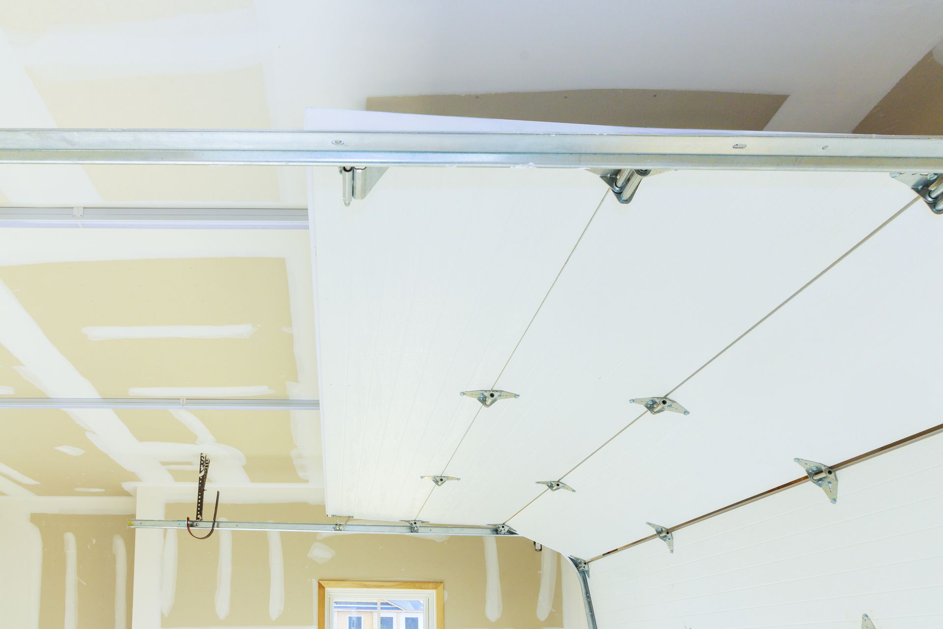 Garage ceiling under construction, drywall and support cables visible. Beige and white colors.