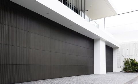 Dark, textured garage door on modern home exterior with white accents and pavers.