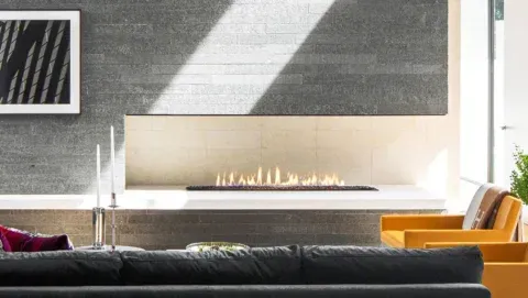 Modern living room with fireplace, gray stone wall, minimalist design, yellow chair, black couch.