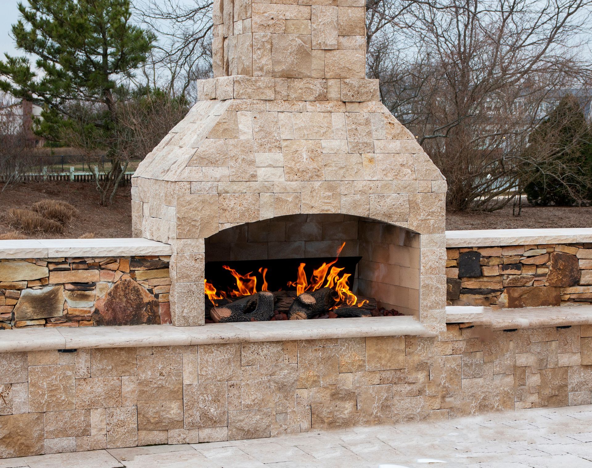 Stone outdoor fireplace with burning logs.