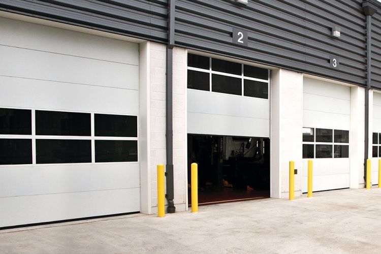 Exterior of a building with three garage doors; one open. White doors with dark-tinted windows. Yellow posts. Concrete floor. Exterior of a building with three garage doors; one open. White doors with dark-tinted windows. Yellow posts. Concrete floor.