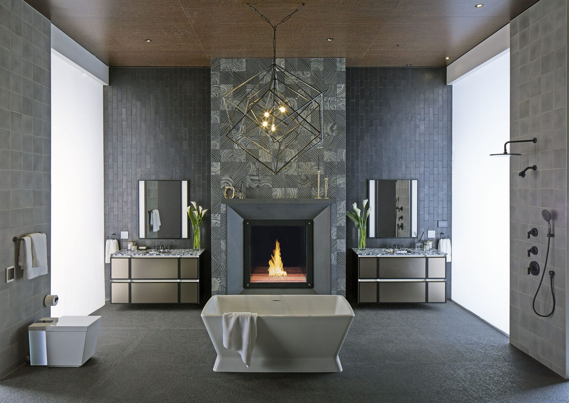 Modern bathroom with fireplace, two vanities, and a freestanding tub. Gray tiles, warm fire.