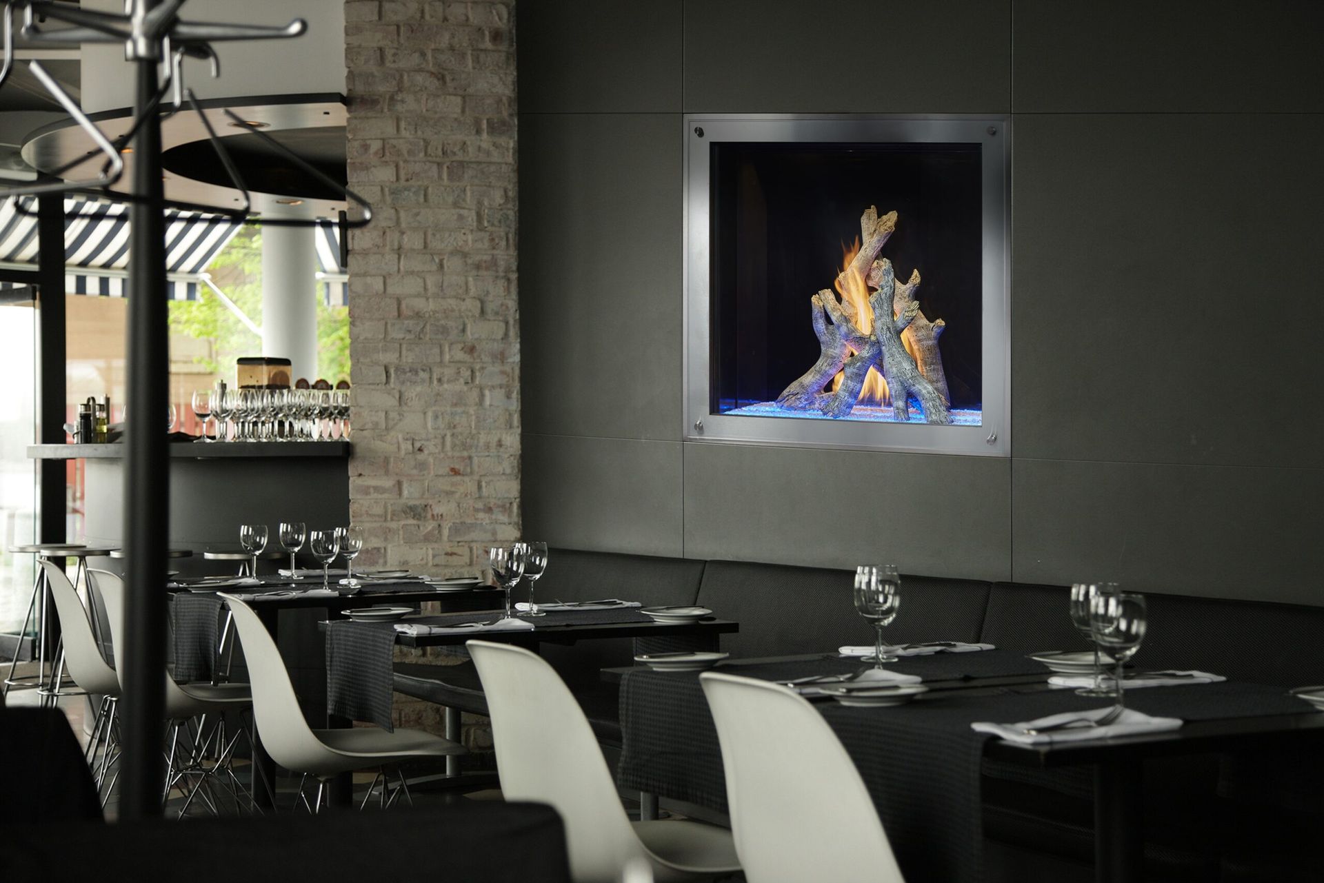 Restaurant dining area with a fireplace in the wall. Tables set with black tablecloths and white chairs.