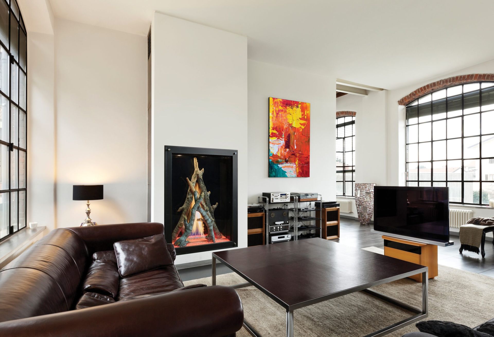 Living room with fireplace, leather couch, and large windows. Modern decor with abstract art. Living room with fireplace, leather couch, and large windows. Modern decor with abstract art.