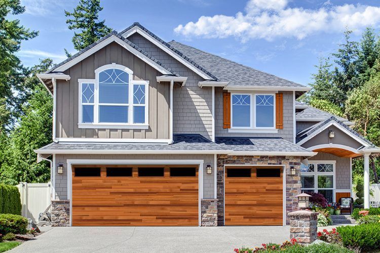 Two-story house with brown garage doors, gray siding, and a landscaped yard under a blue sky. Two-story house with brown garage doors, gray siding, and a landscaped yard under a blue sky.