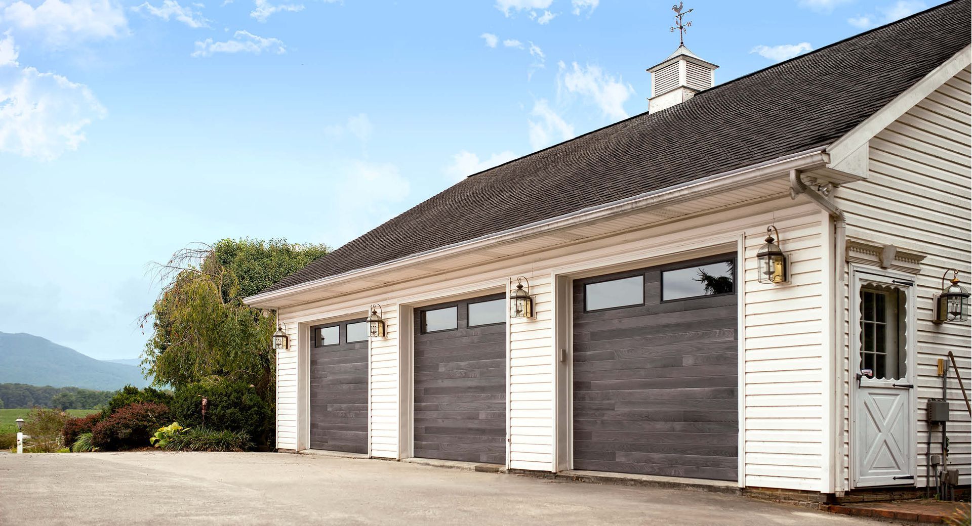 Three-car garage with gray doors, white siding, and a small door, under a blue sky.