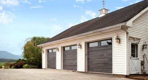Three-car garage with gray doors, white siding, and a small white door.