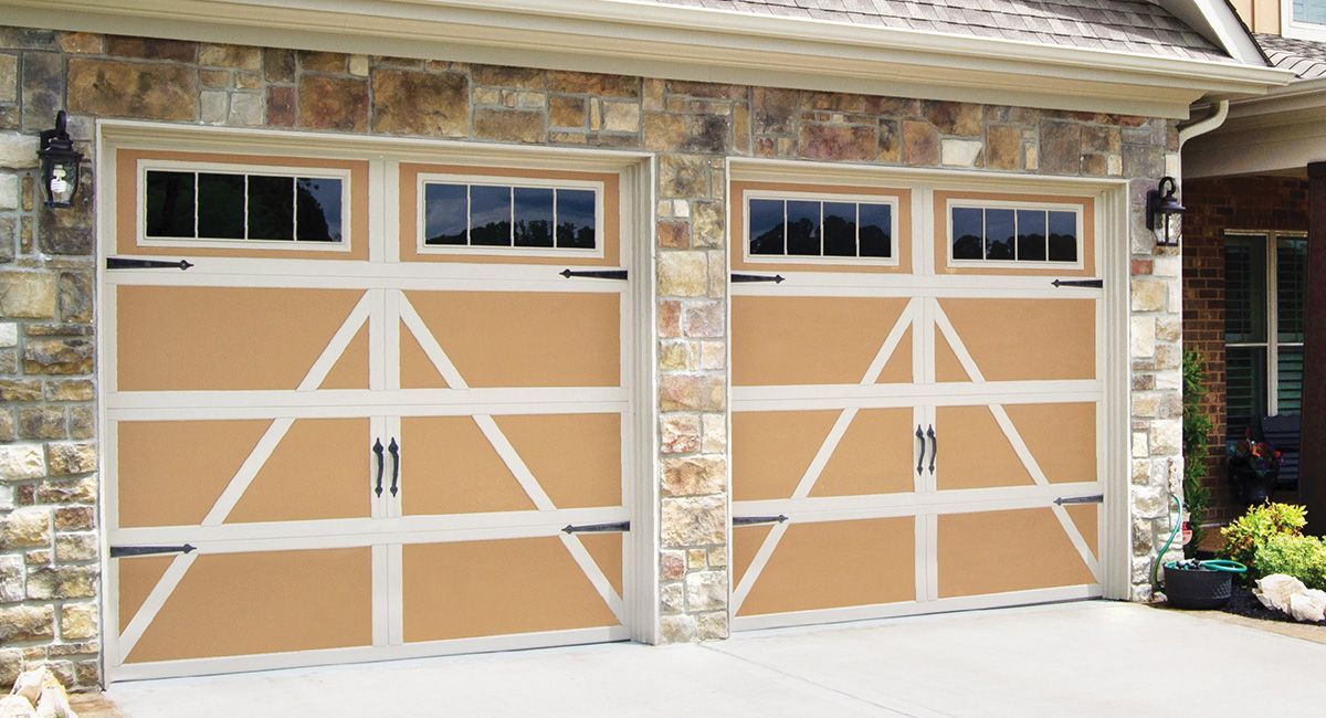 Tan garage doors with white accents, small windows, and stone facade.
