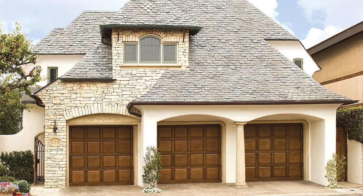Stone and stucco home with three wooden garage doors and slate roof.