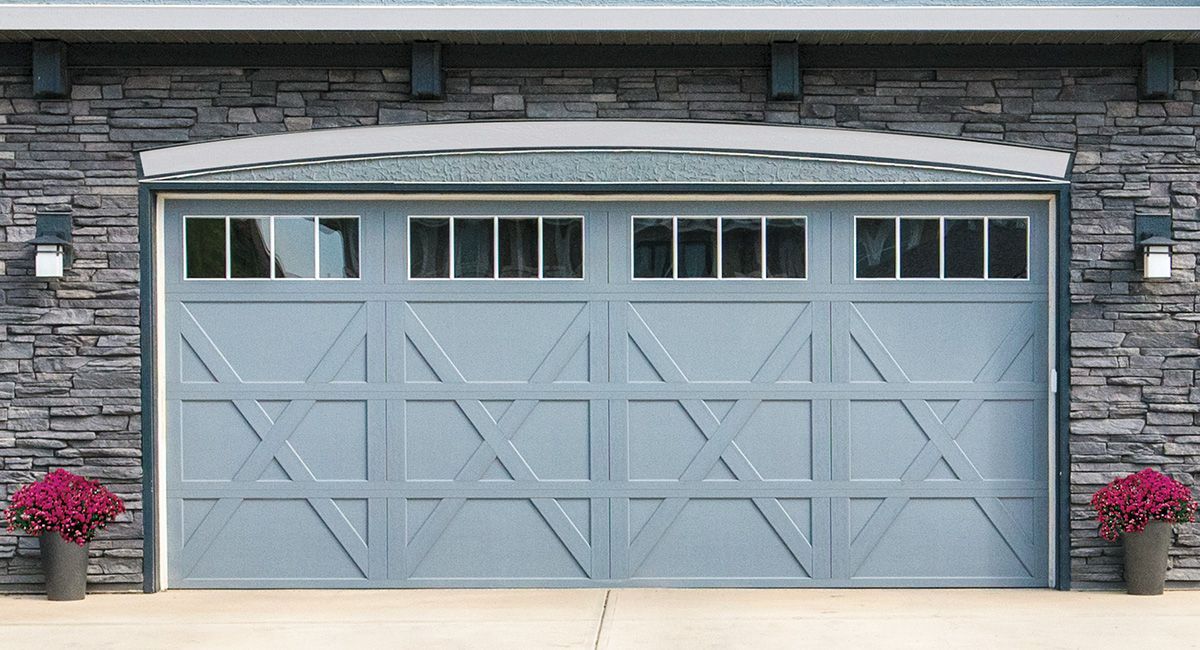 Blue garage door with windowed top, set in stone wall, with planters and outdoor lights.