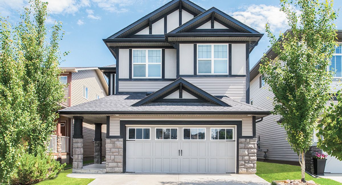 Two-story house with gray siding, a garage, and dark trim. Landscaping with green trees in front.