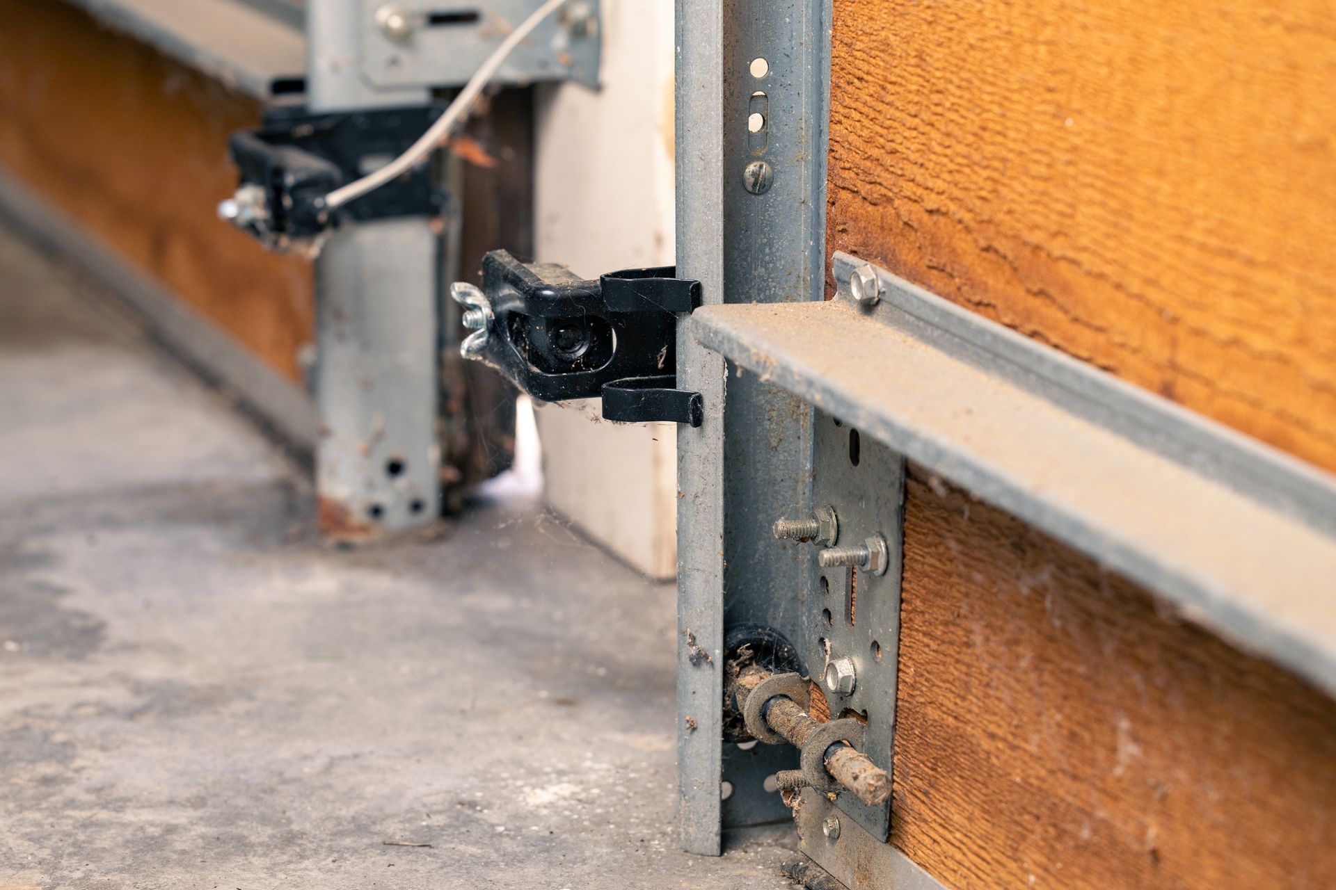 Garage door mechanism, with metal track, hardware, and sections of wood paneling. Dusty concrete floor visible.