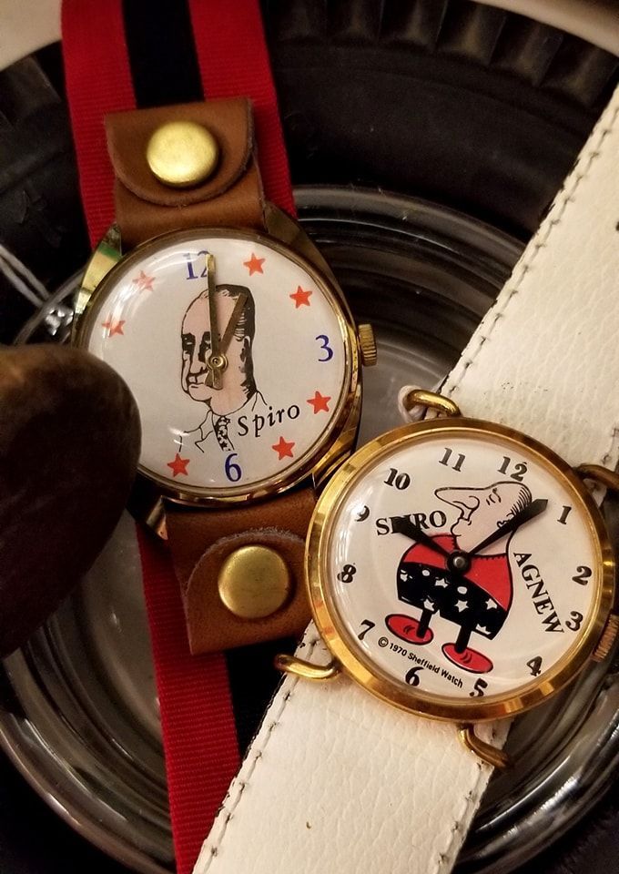 Two vintage Spiro Agnew novelty wristwatches with cartoon illustrations on their faces, resting on a dark surface.