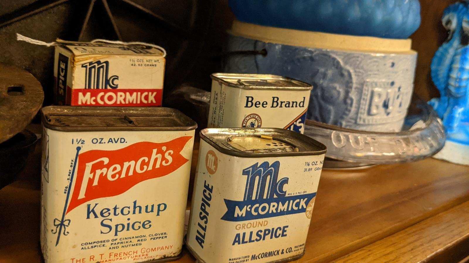 Vintage metal spice tins, including French's and McCormick brands, sitting on a wooden shelf next to a blue ceramic pot.