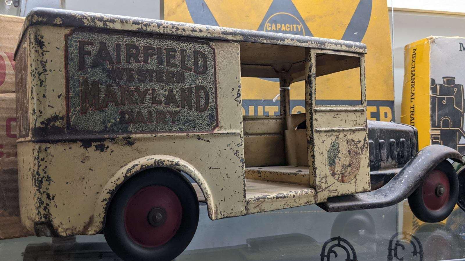 A weathered, vintage toy delivery truck painted cream with red wheels, labeled