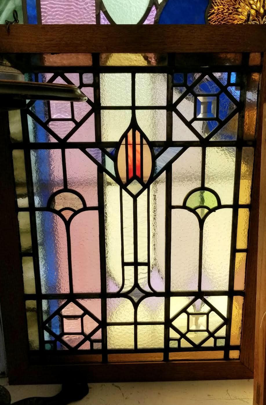 A stained glass window with a central floral motif in red, surrounded by geometric patterns in pink, blue, and yellow.