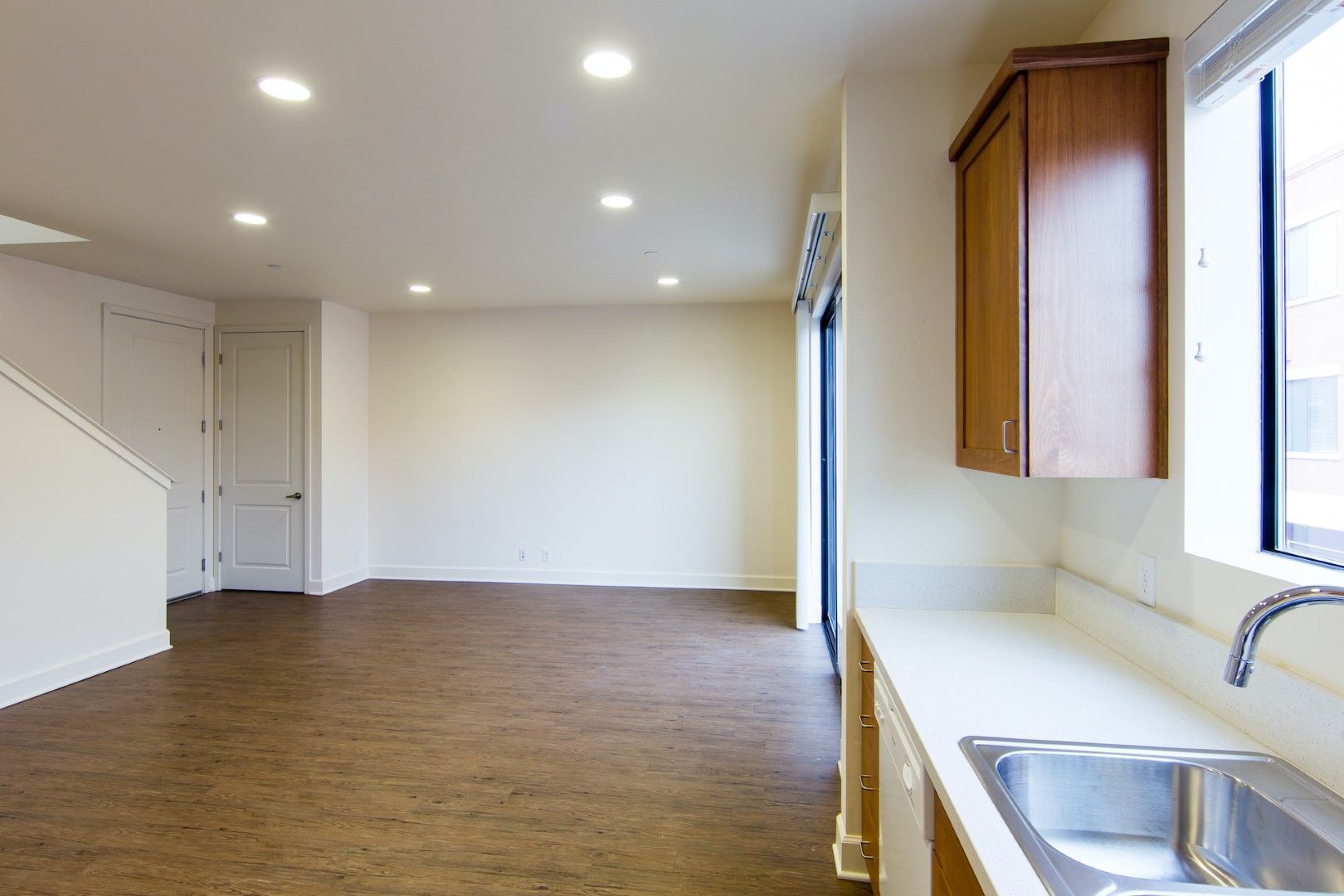 An empty kitchen with a sink , cabinets and a window.