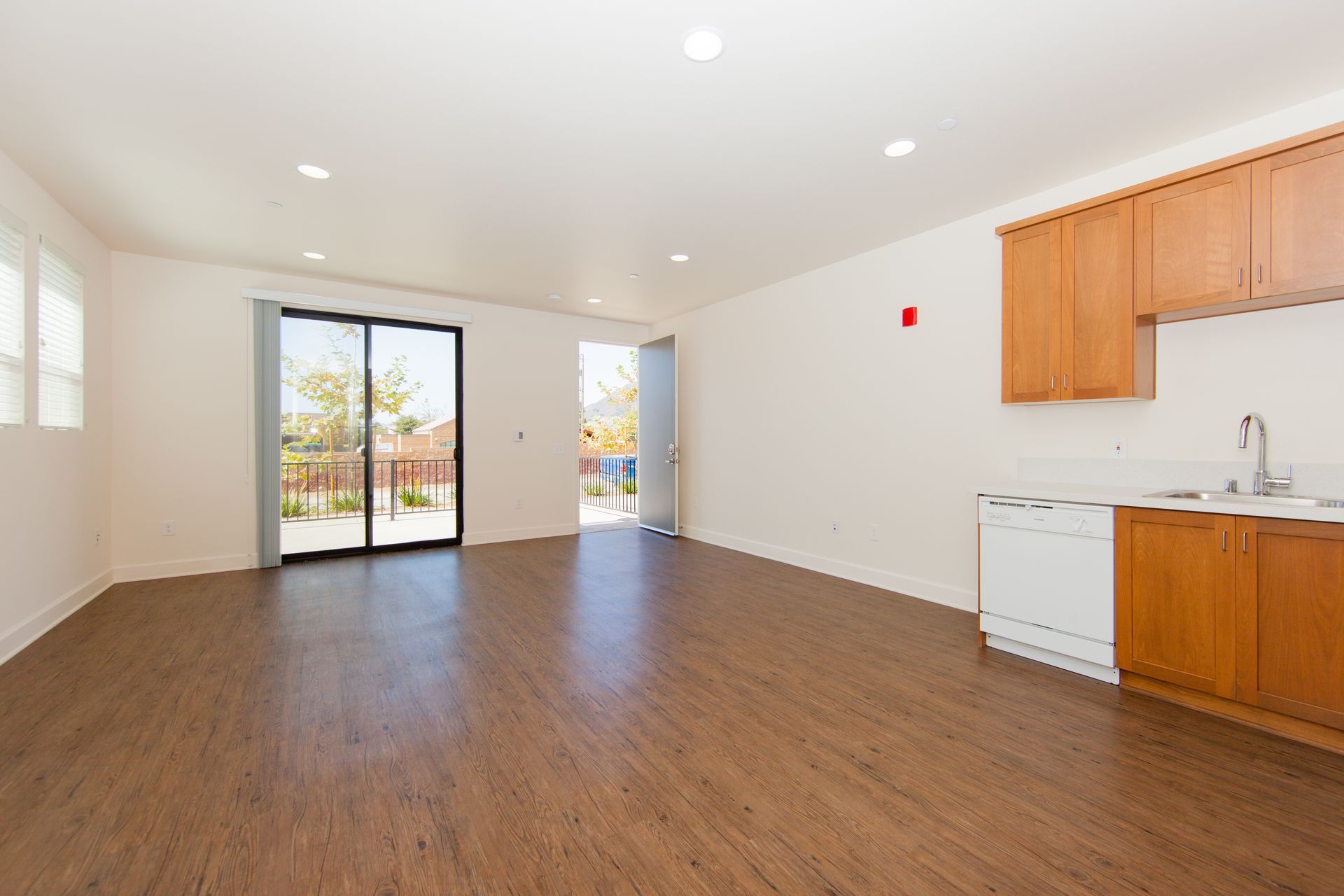 An empty living room with a kitchen and sliding glass doors.