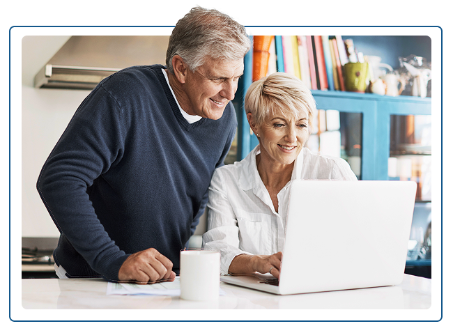 Elderly couple looking at laptop together in kitchen, smiling.