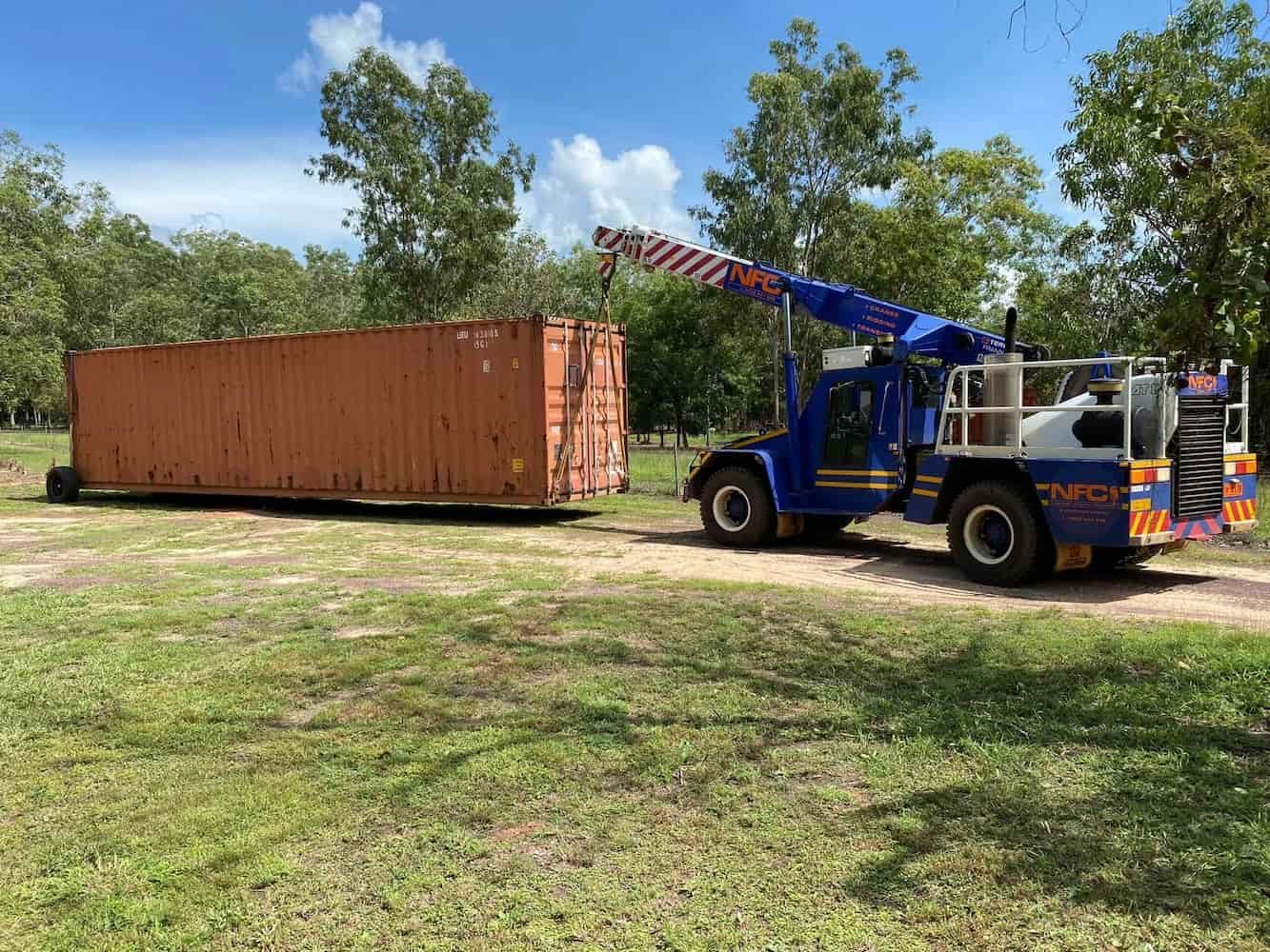 A Blue Tow Truck Is Towing a Large Orange Container in A Grassy Field — Northern Franna Cranes NT in Noonamah, NT