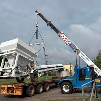 Crane lifting heavy equipment onto a trailer under a cloudy sky.