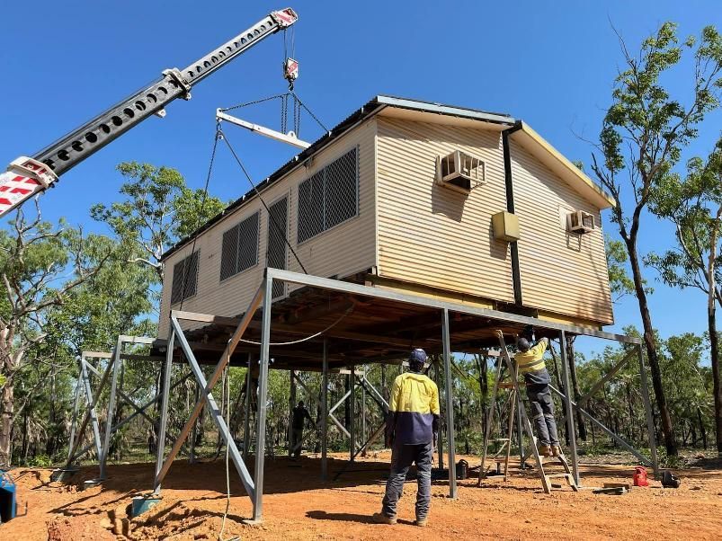A Crane Is Lifting a House on Stilts in The Dirt — Northern Franna Cranes NT in Noonamah, NT