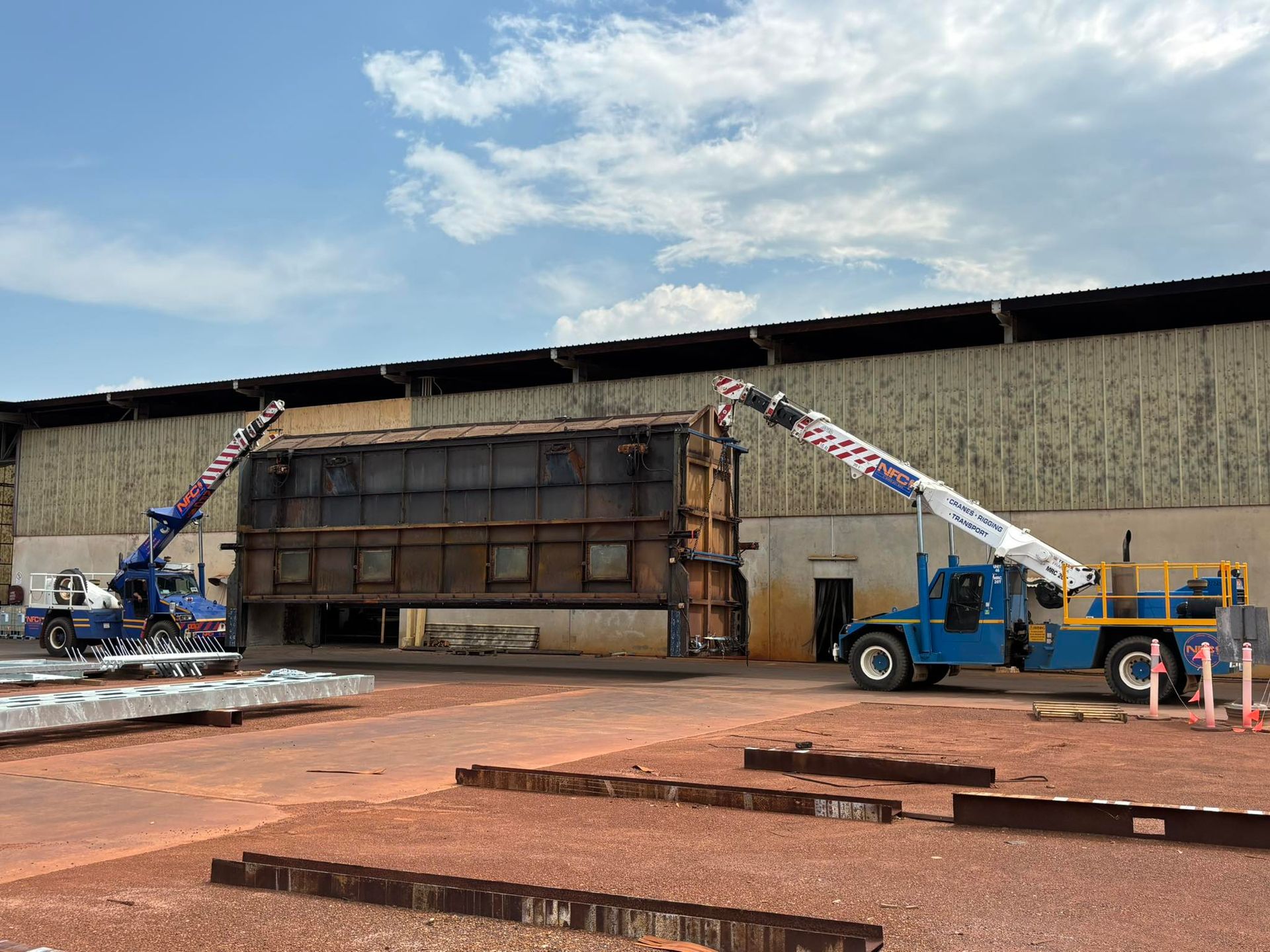 A Crane Is Lifting a Large Piece of Metal in Front of A Building — Northern Franna Cranes NT in Noonamah, NT