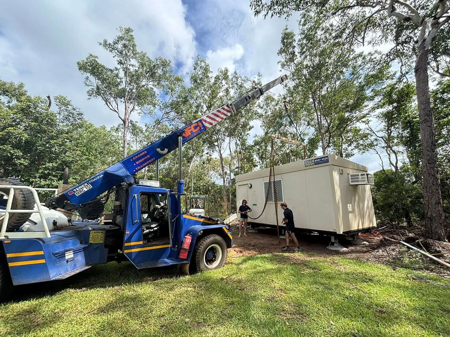 A Crane Lifting a Tan Building Module in a Wooded Area