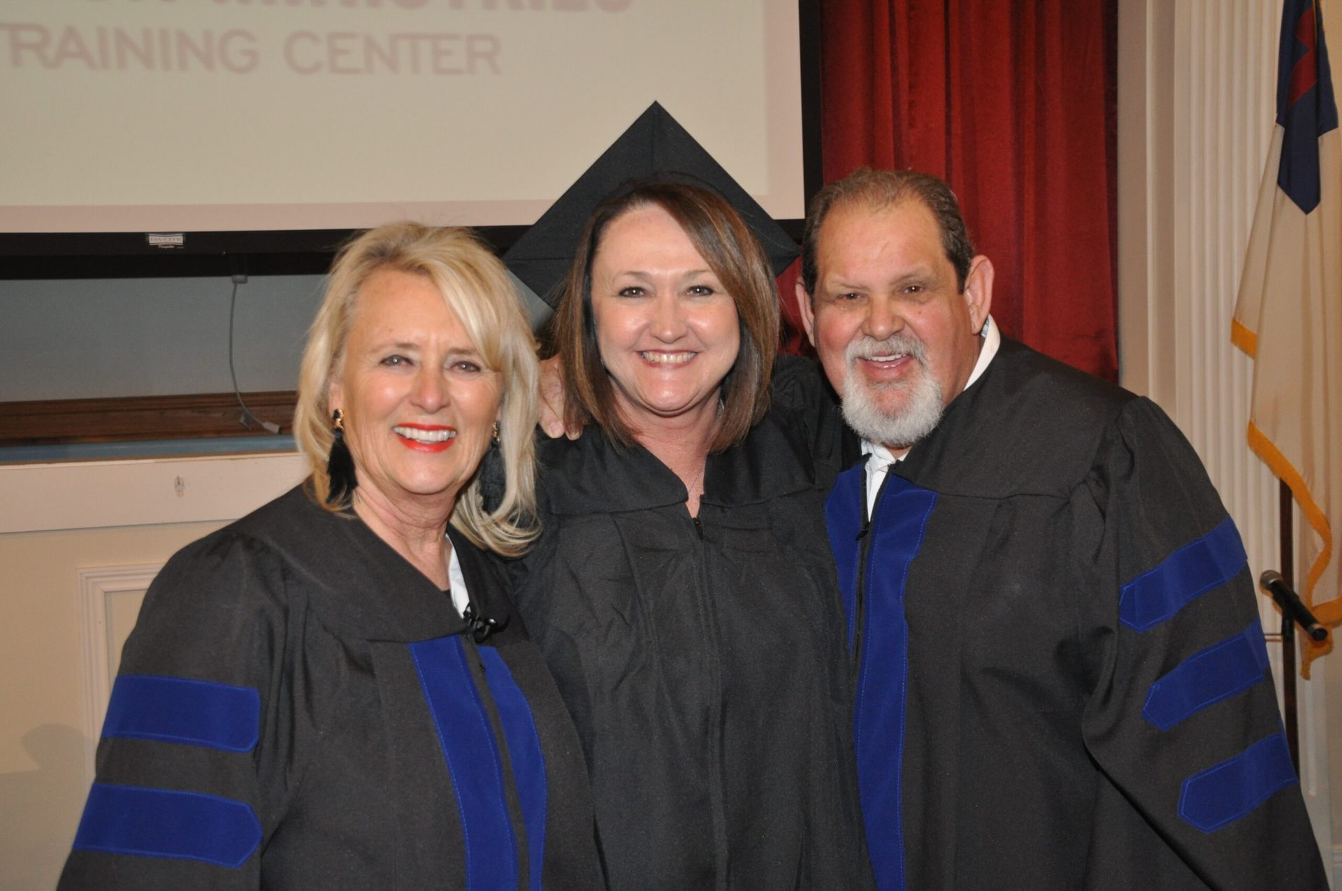 Three people in graduation gowns smile, posing in a room.