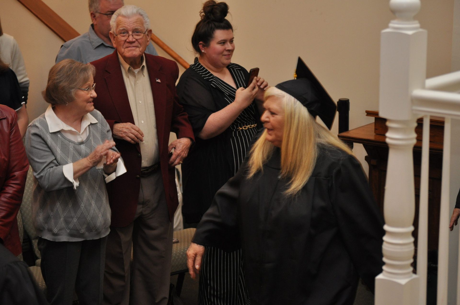 Graduate in cap and gown descends stairs, accompanied by supportive family.
