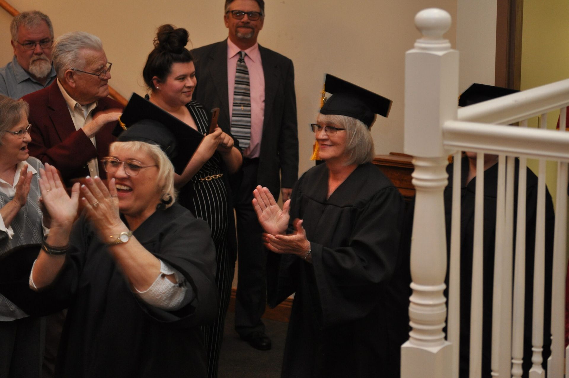 People clapping for two graduates wearing gowns and caps on a staircase.