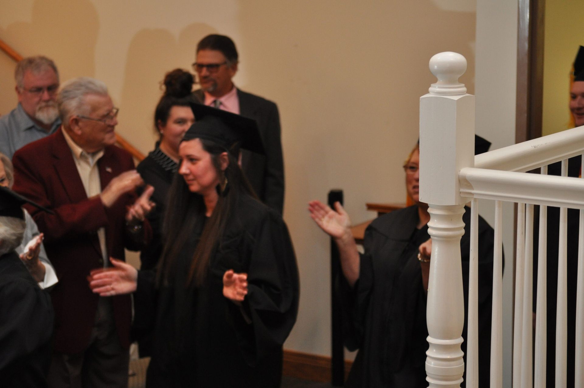 Graduates in black gowns and caps, greeted by well-wishers on a staircase landing.