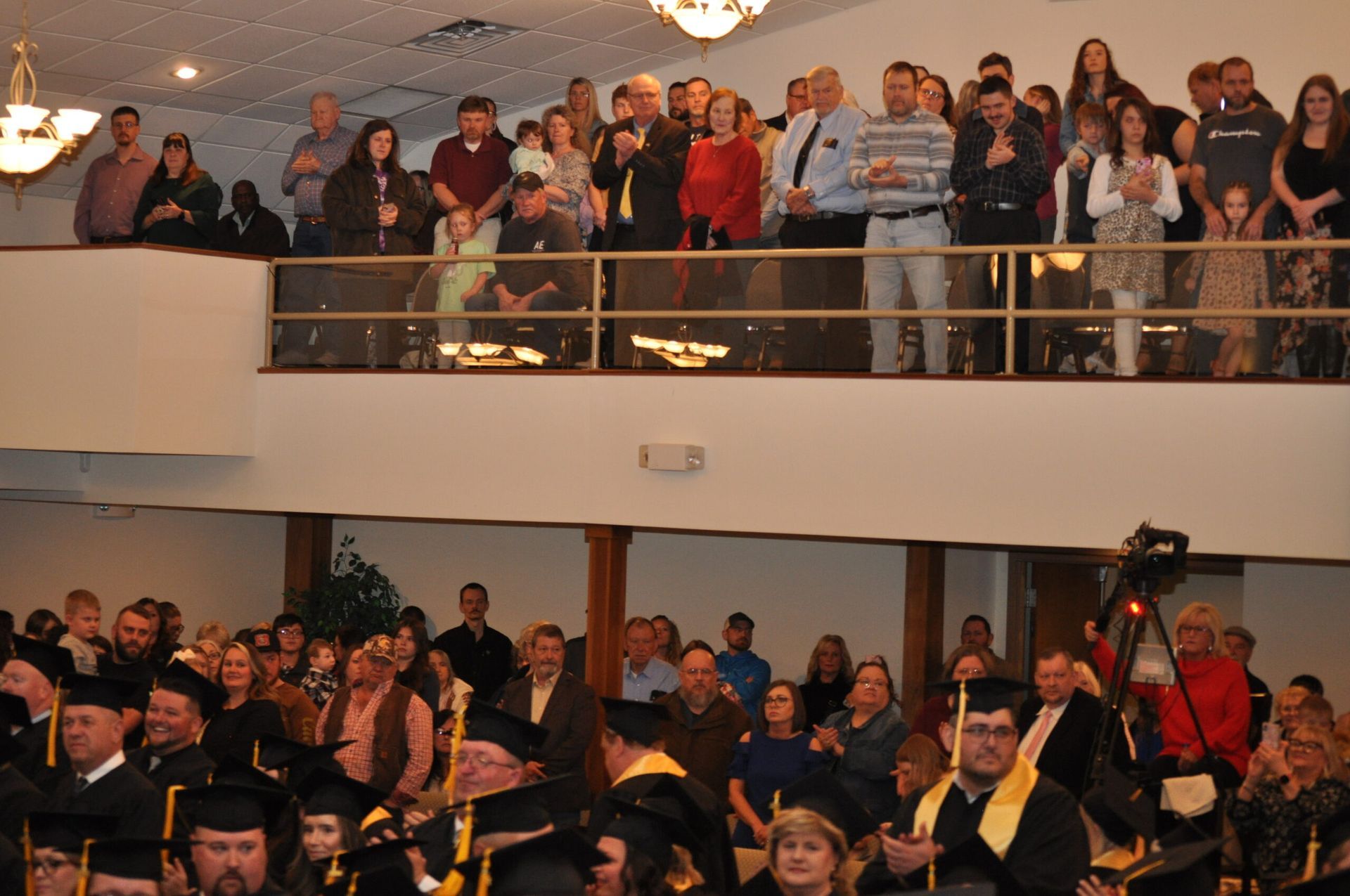 Audience watching graduation ceremony from a balcony and ground floor.