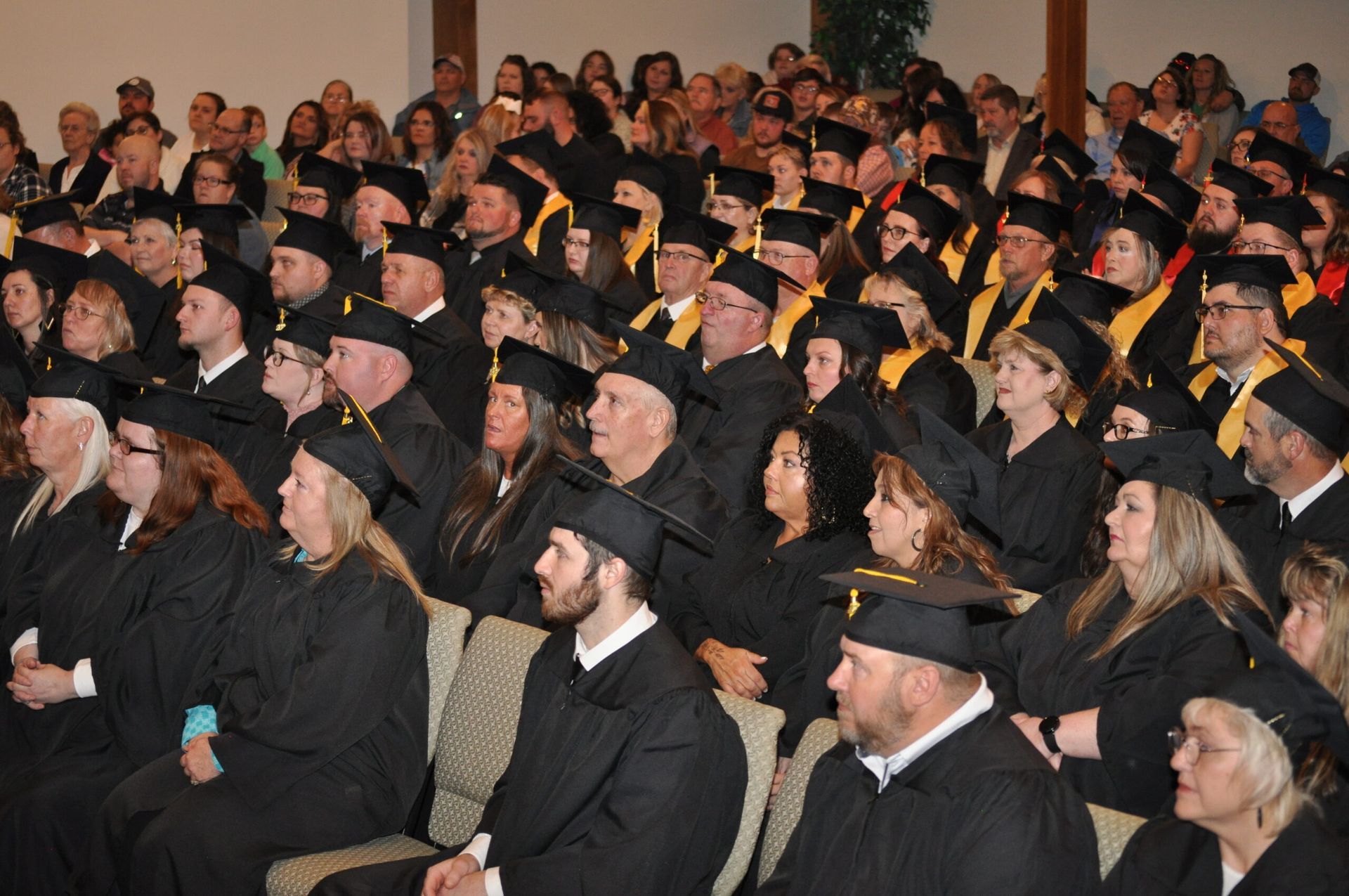 Graduation ceremony: graduates in black caps and gowns seated in an auditorium.