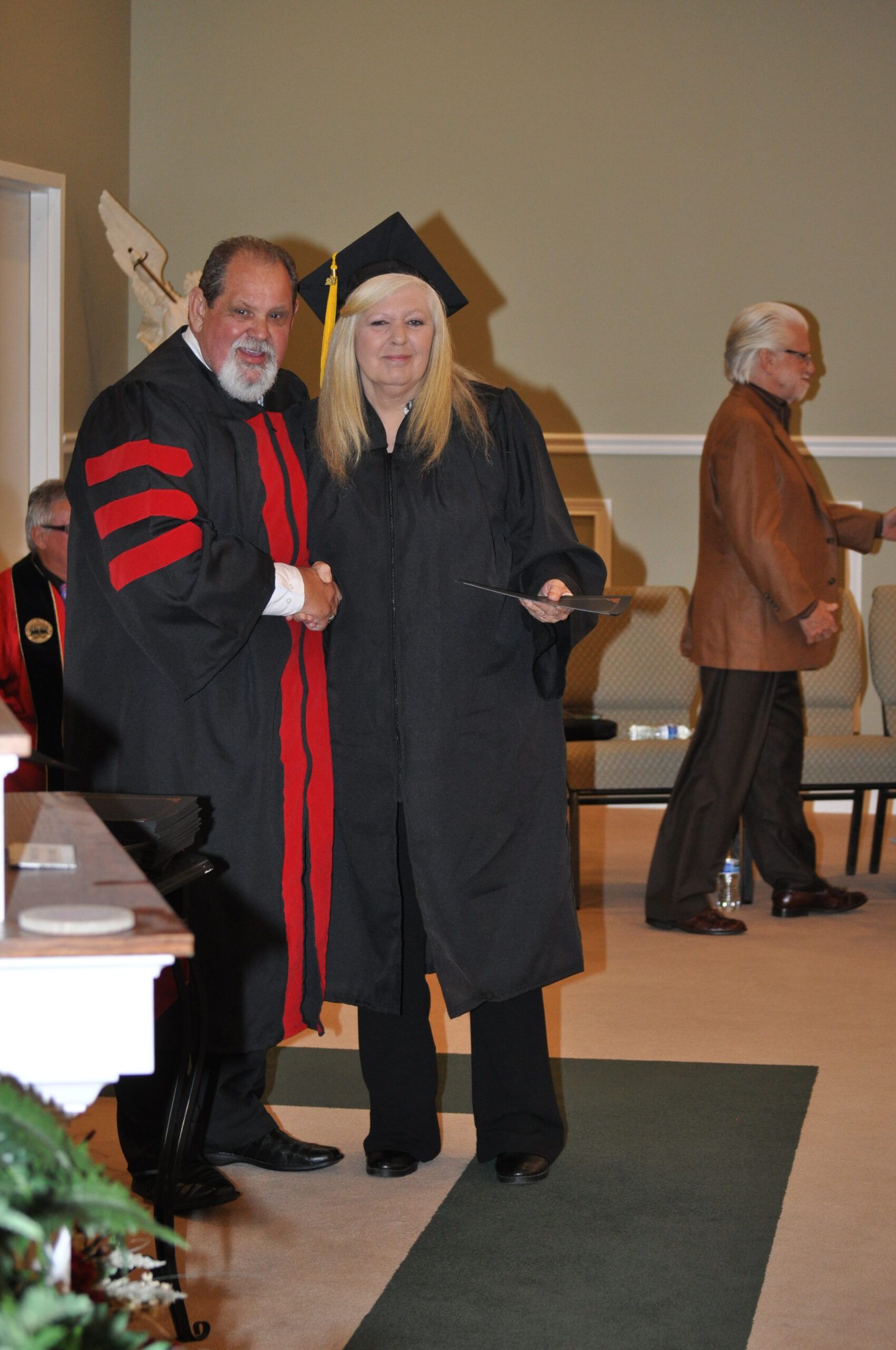 Graduation ceremony: a woman in cap and gown receives a diploma from a man in academic regalia.