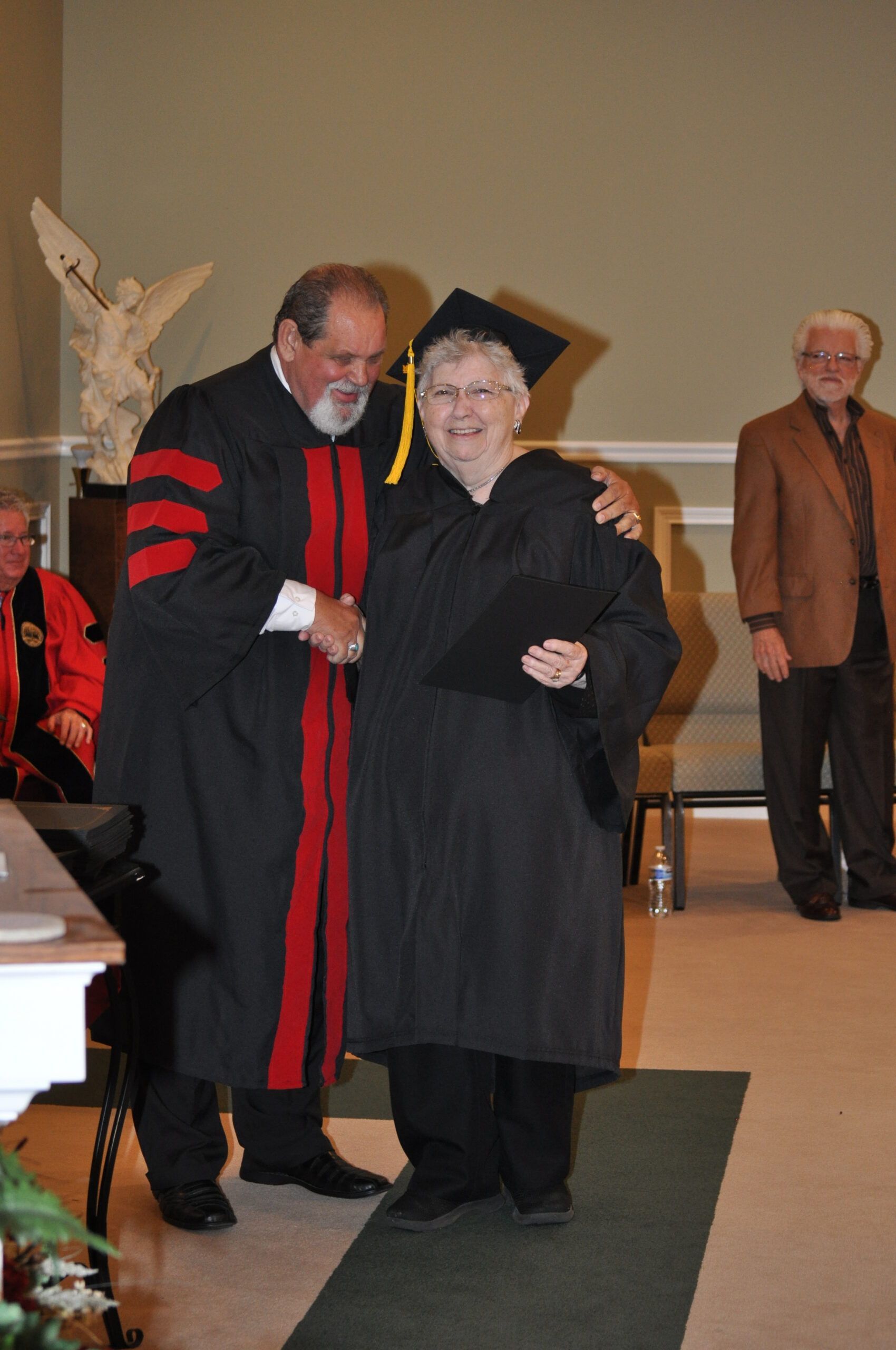 Man in academic robe shakes hands with graduate wearing cap and gown.