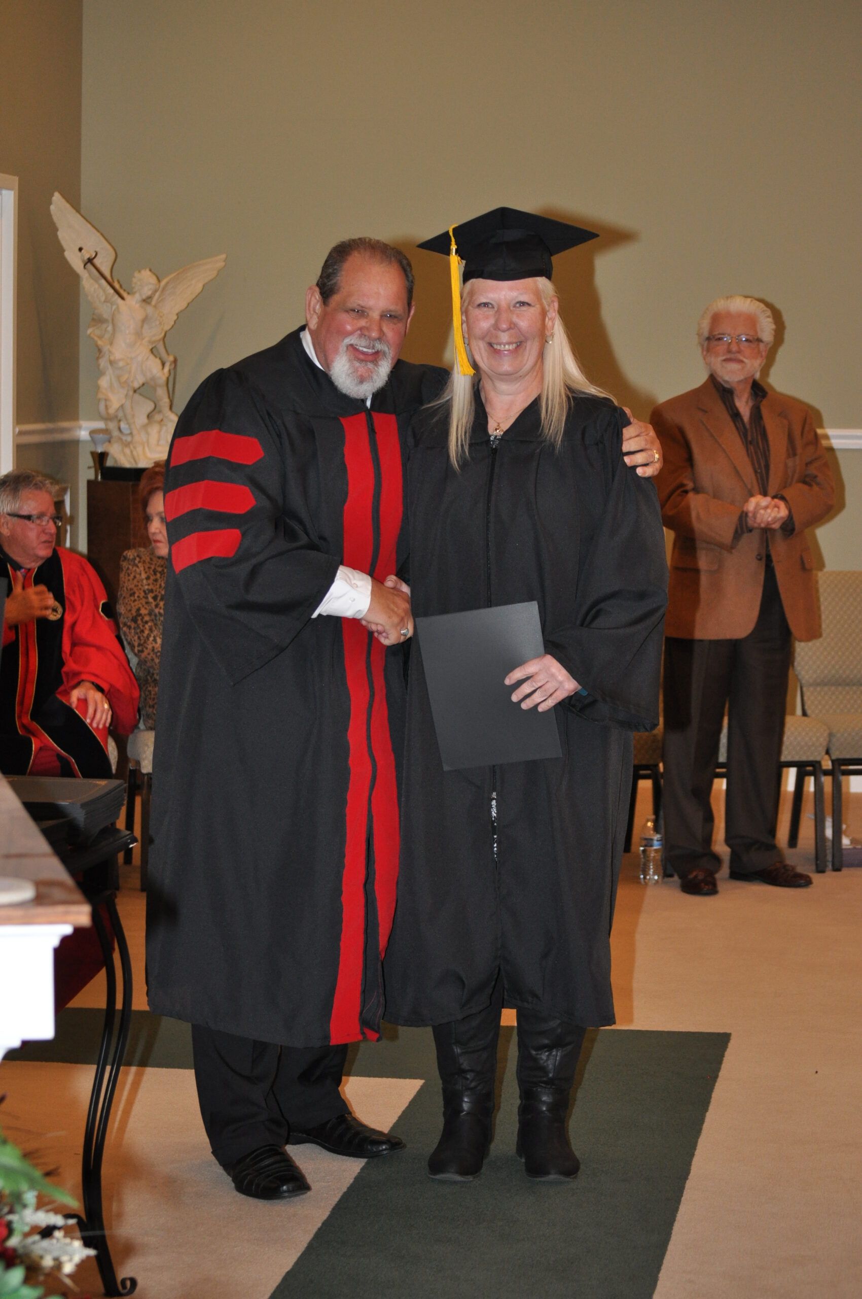 A woman in a cap and gown shaking hands with a robed man at a graduation ceremony.