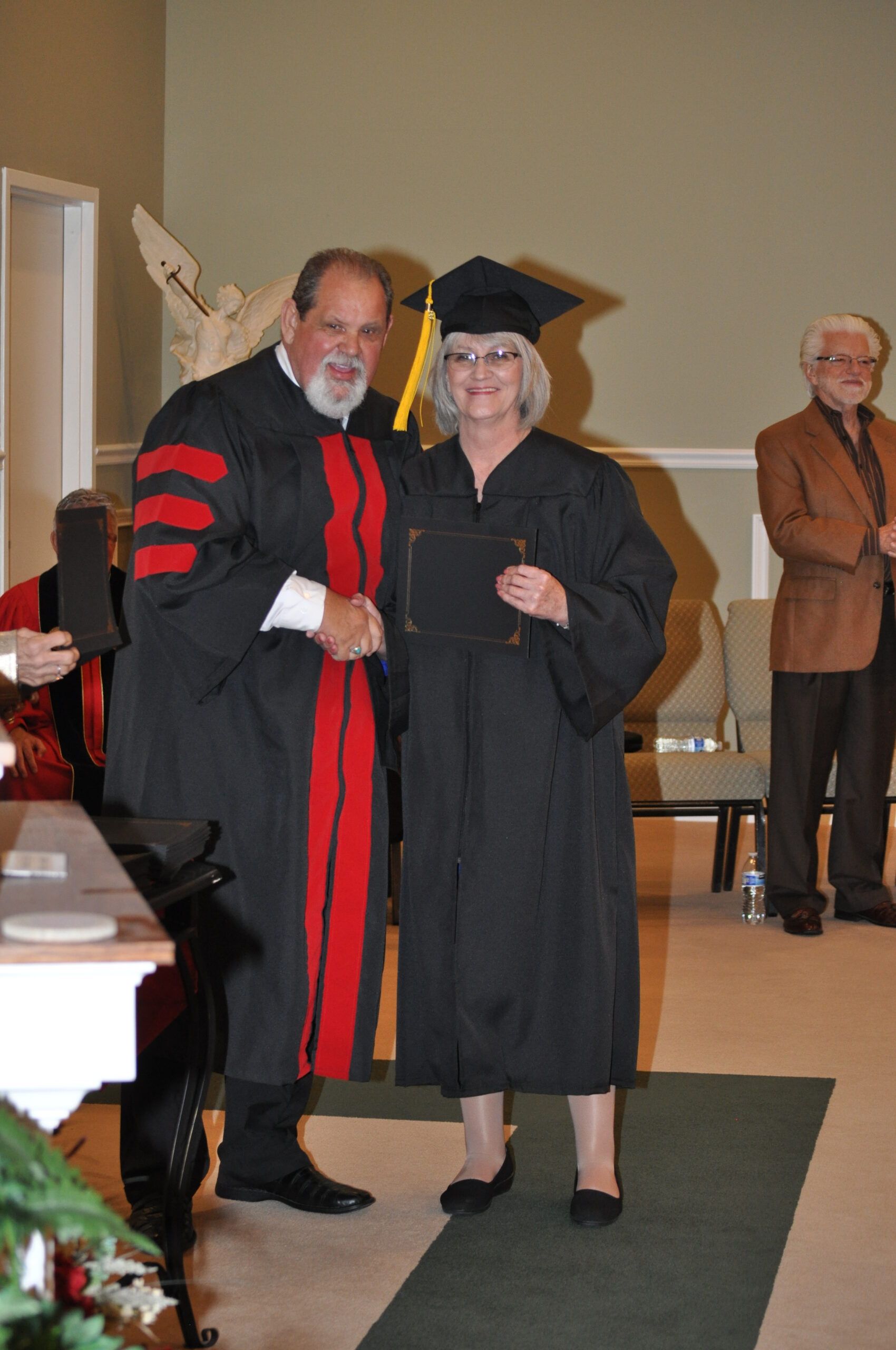 Man in academic regalia shakes hands with woman in cap and gown at a graduation.