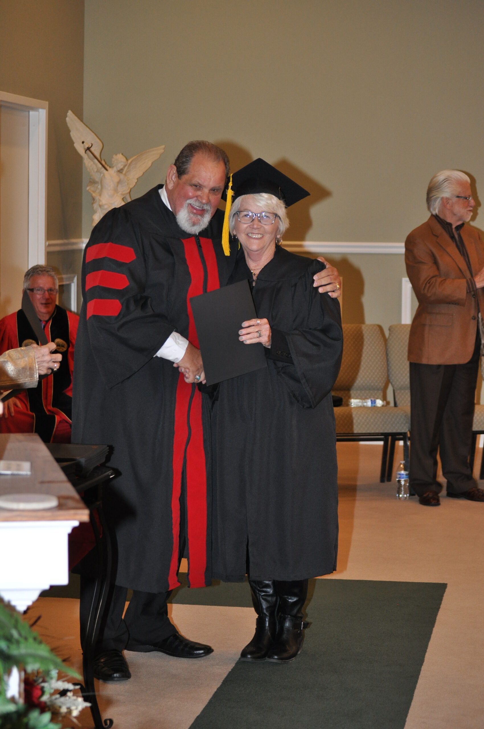 Professor in academic regalia presents diploma to a graduate wearing a cap and gown. They smile at each other.
