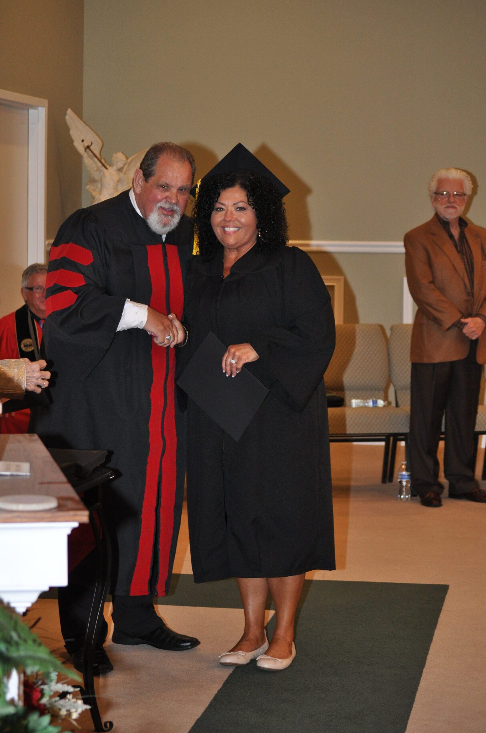 Woman in graduation gown receives diploma, shakes hands with official at ceremony.