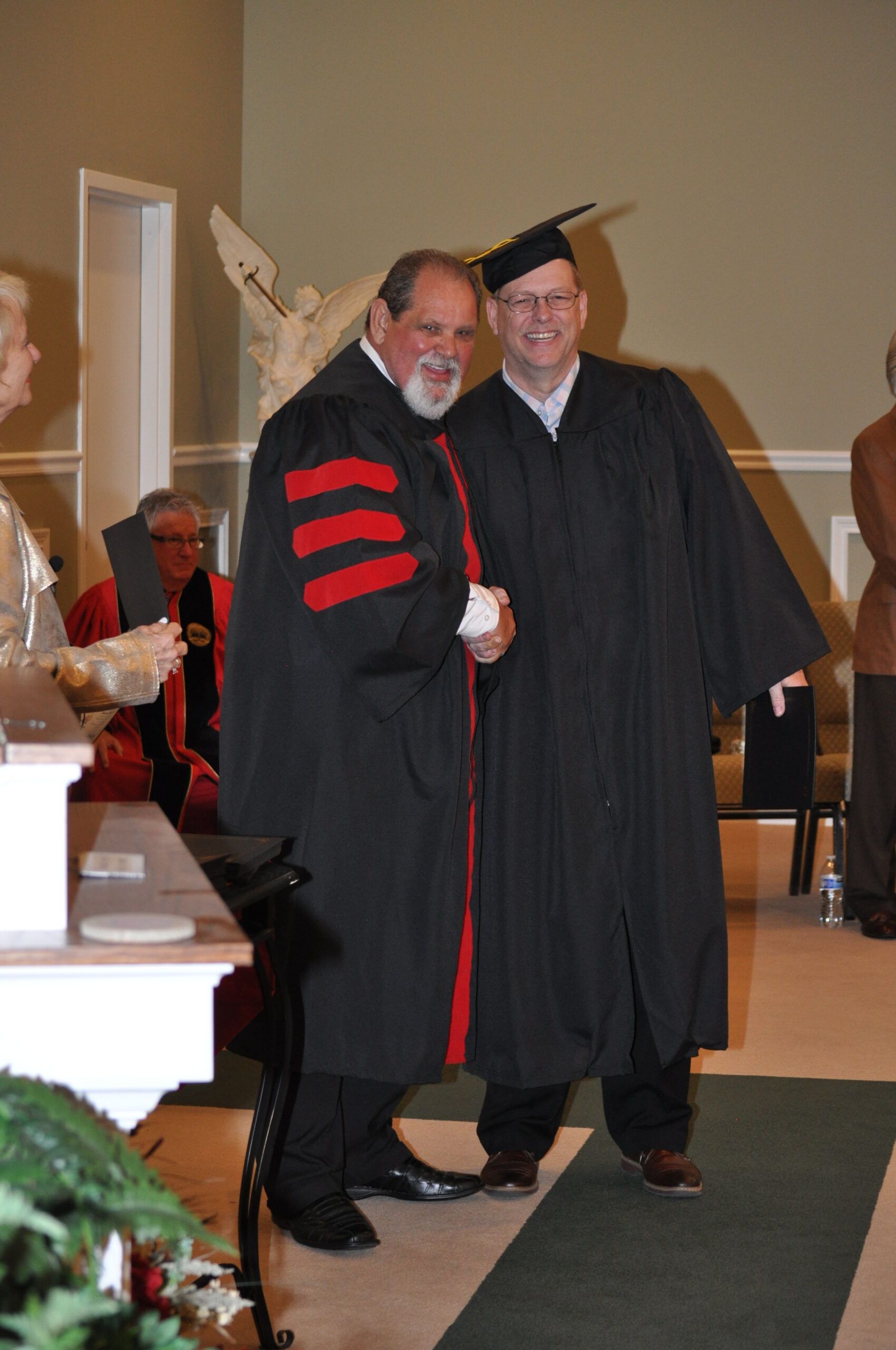 Man in cap and gown shakes hands with a man in academic robes at a graduation.