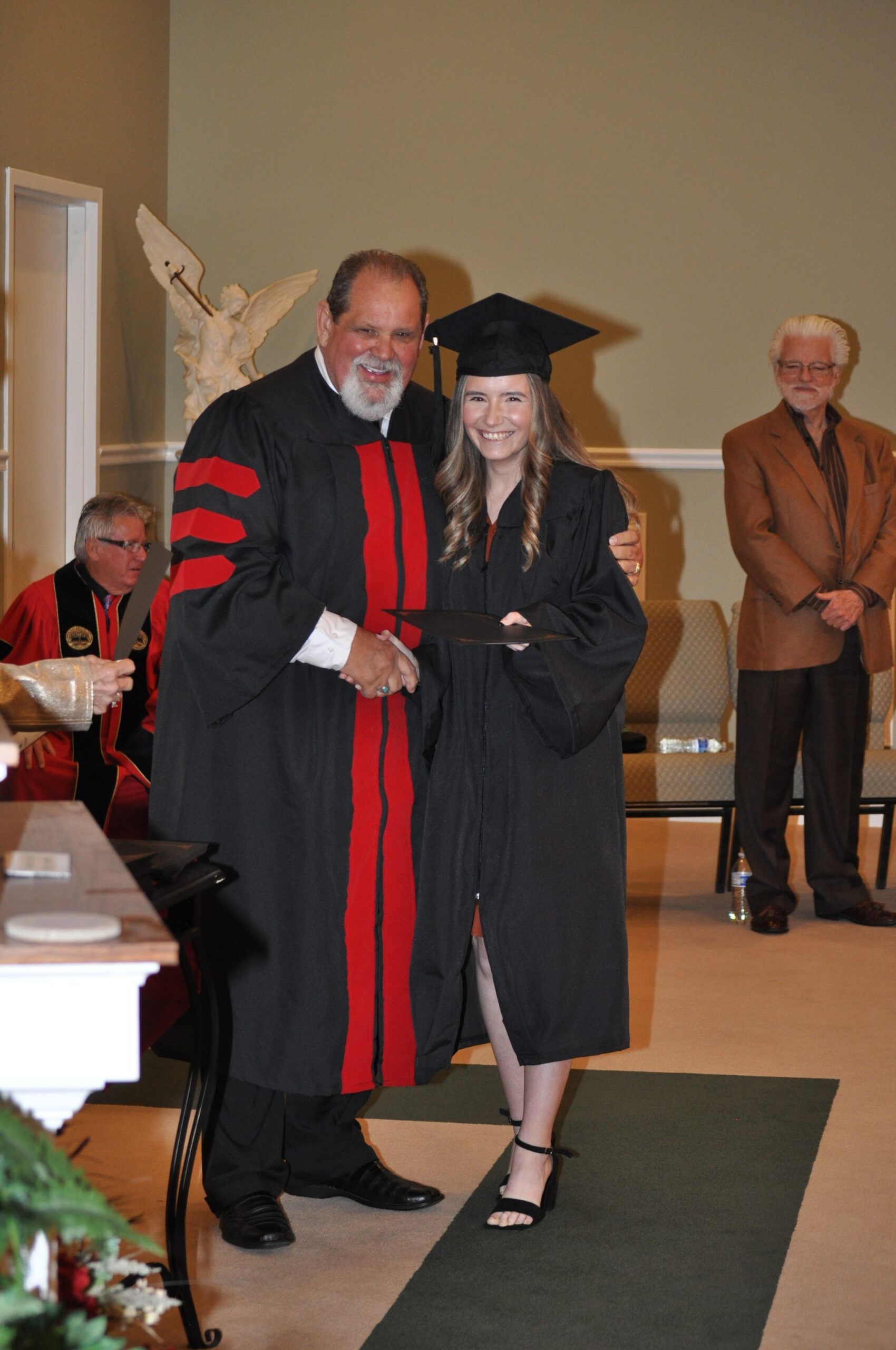 A graduate in cap and gown shakes hands with a man in academic robes at a ceremony.
