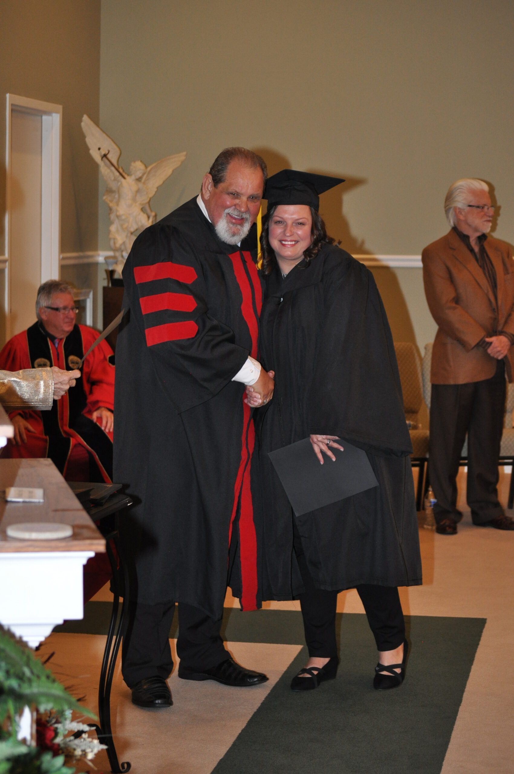 Person in graduation gown shaking hands with another person in a similar gown.